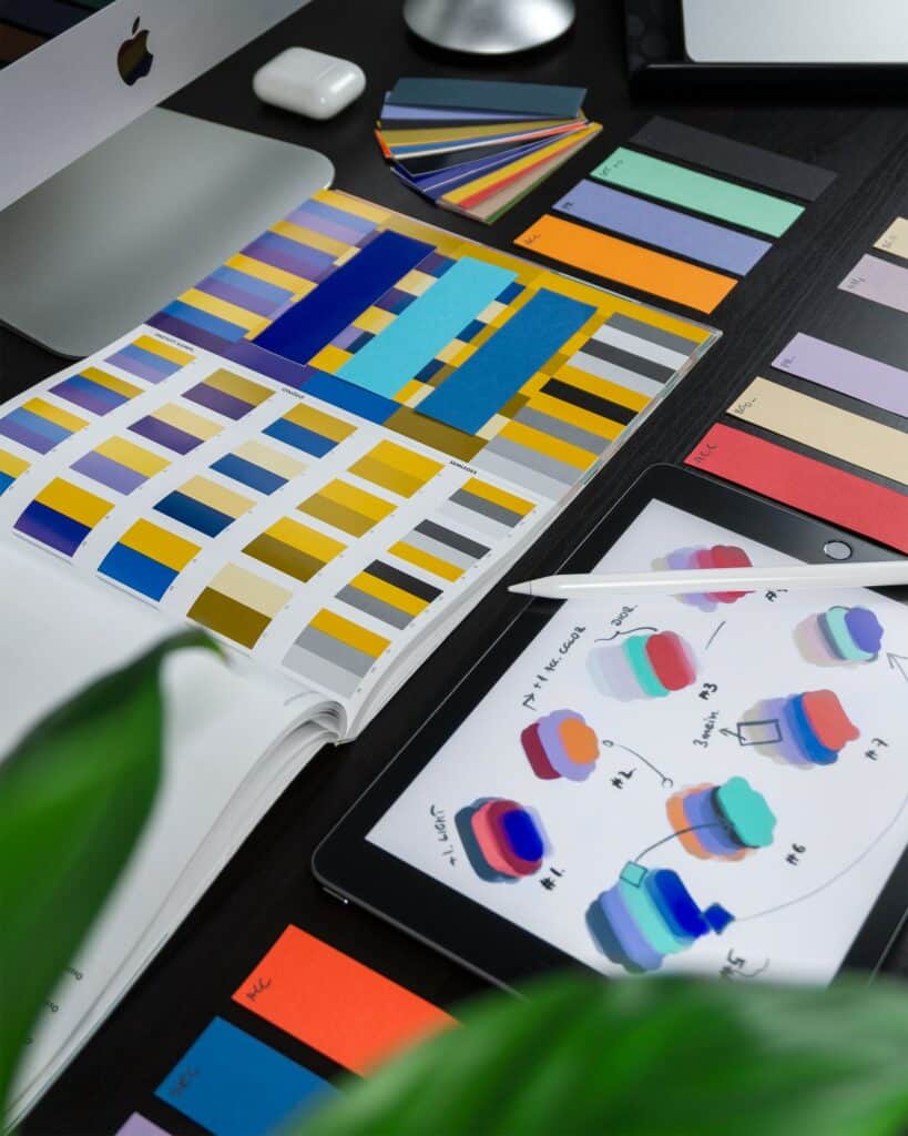 A digital tablet displaying color palette concepts next to printed brand style guides and swatches on a designer's desk.