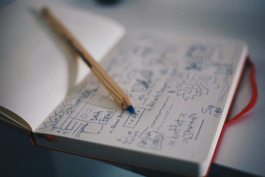 A close-up of a pencil resting on a notebook filled with hand-drawn website wireframe sketches and brand strategy notes.