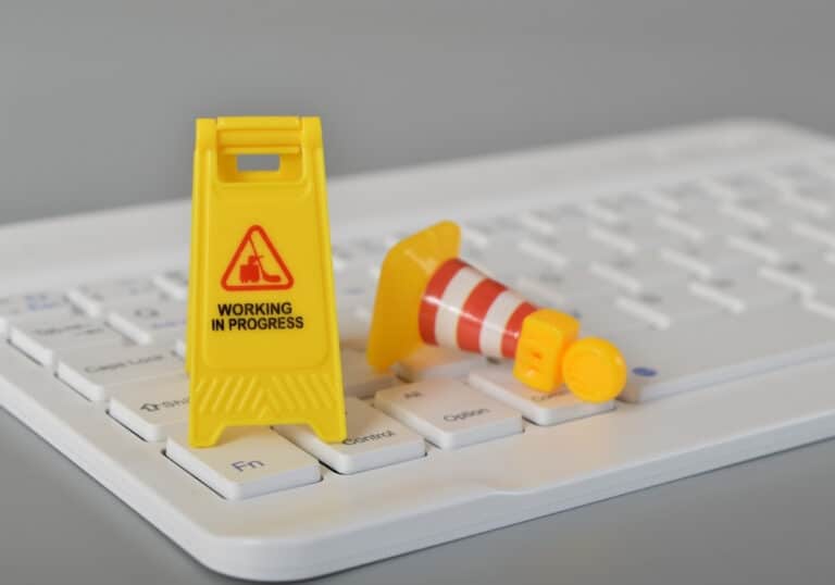 A miniature yellow "Working in Progress" sign and a small orange traffic cone sitting on top of a white computer keyboard, symbolizing website maintenance.