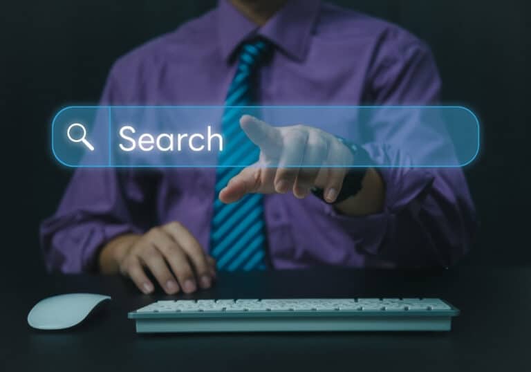 A businessman pointing toward a glowing digital holographic search bar hovering over a computer keyboard, representing AI search engine optimization.