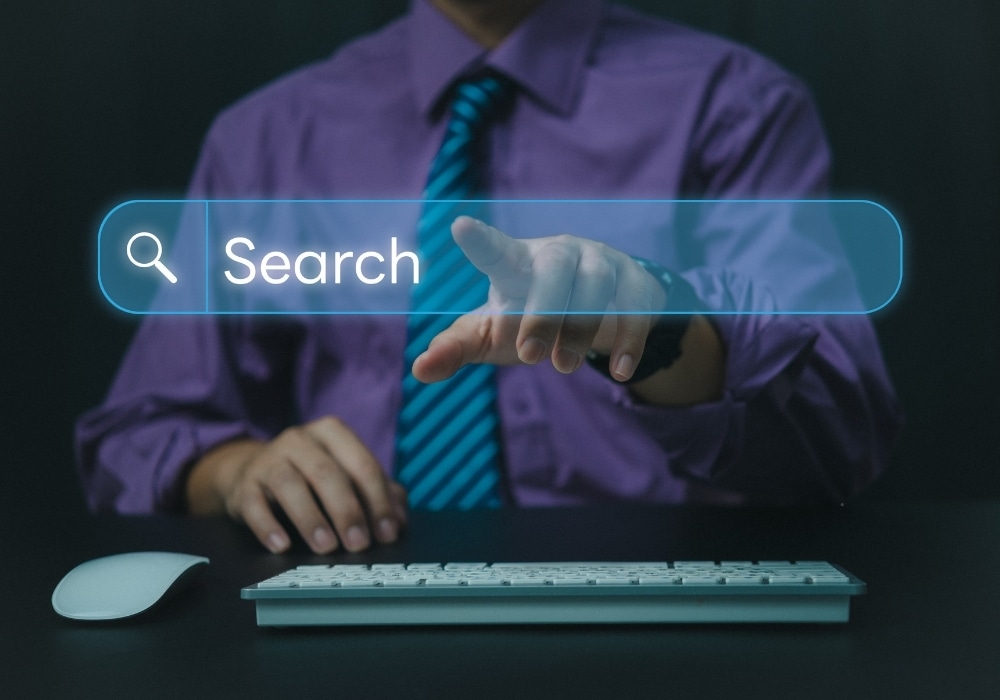 A businessman pointing toward a glowing digital holographic search bar hovering over a computer keyboard, representing AI search engine optimization.