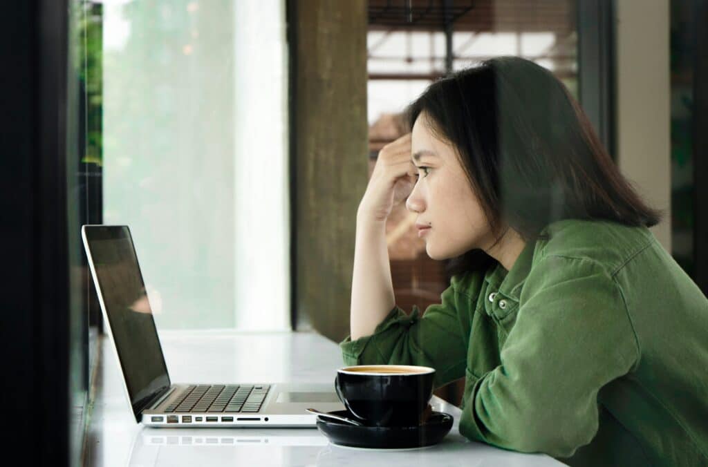 A thoughtful business owner leaning on her hand while looking at a laptop screen, representing the frustration of unguided marketing.