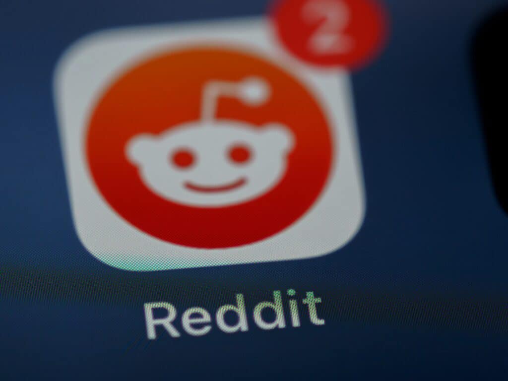 A close-up macro shot of the Reddit mobile application icon on a smartphone screen showing a red notification badge with the number two.
